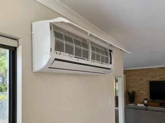 Clean split system with open front panel and visible filters on a beige living room wall in Pacific Pines