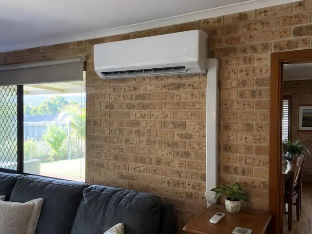 Wall-mounted split system on a brick feature wall in a living room with a garden view in Pacific Pines