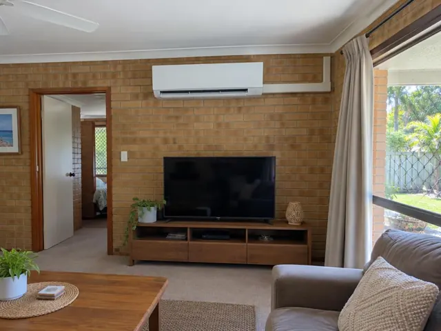 Wall-mounted split system above a TV on a brick feature wall in a living room in Nerang